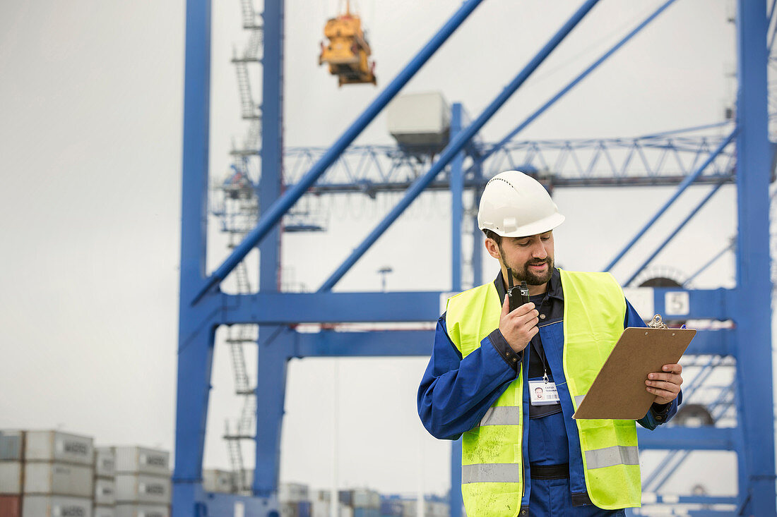 Dock worker with walkie-talkie and clipboard at shipyard