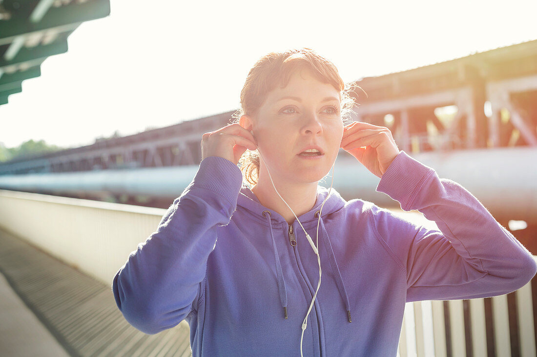 Young runner adjusting headphones, listening to music