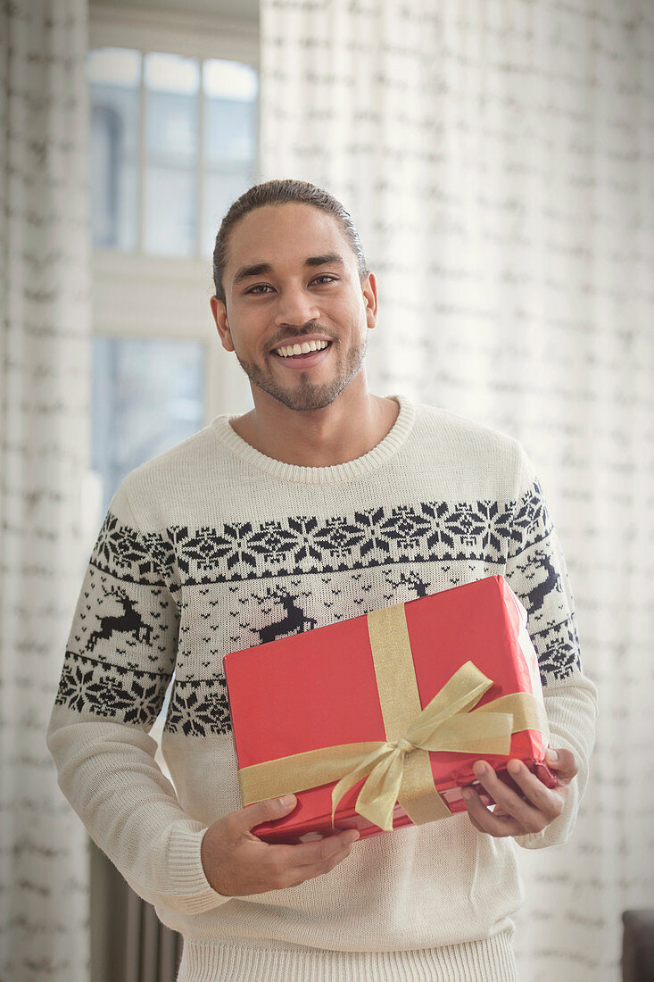 Portrait young man in Christmas sweater holding gift