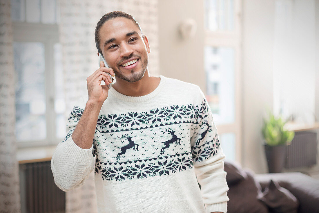 Smiling man in Christmas sweater talking on cell phone
