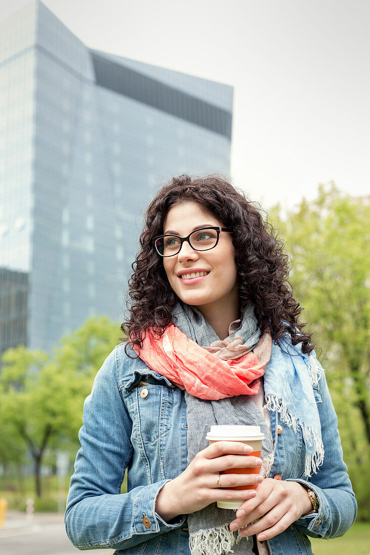 Smiling woman drinking coffee in urban park