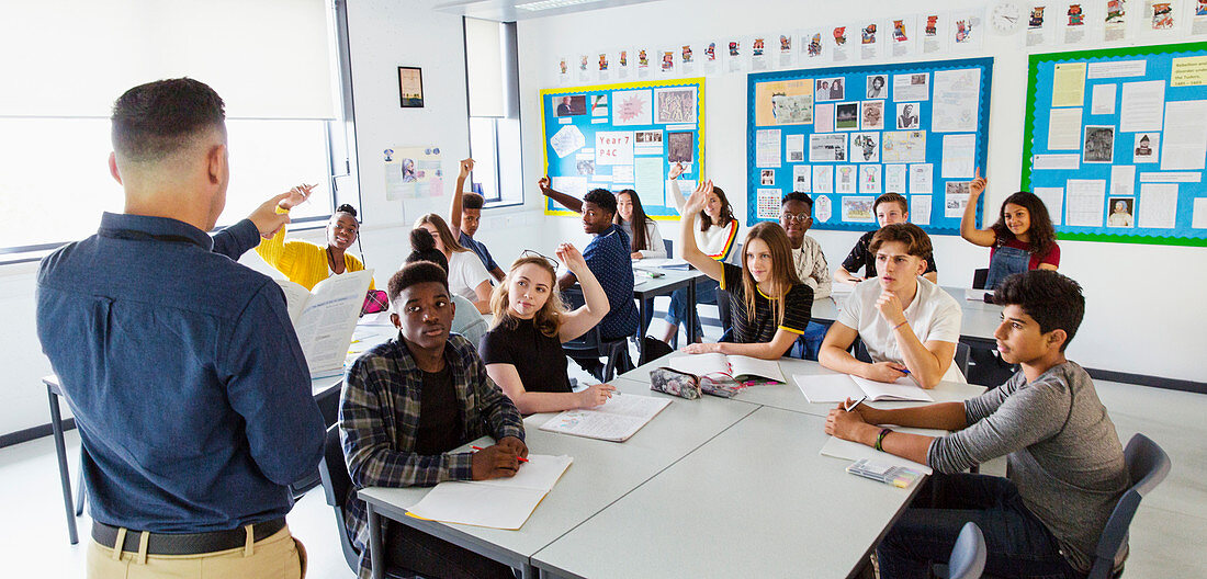 Teacher calling on students with hands raised in classroom