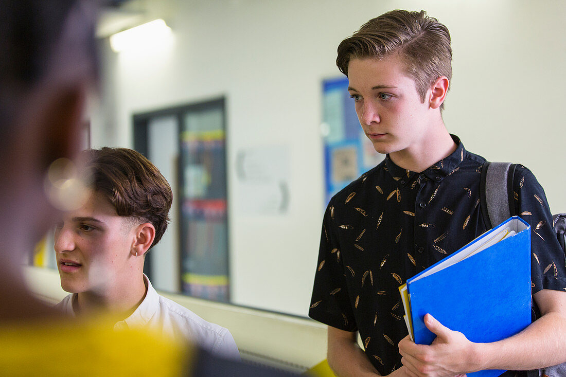 Focused boy student listening to friends in corridor