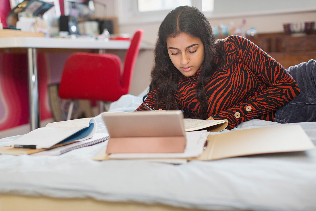 Focused teenage girl doing homework on bed