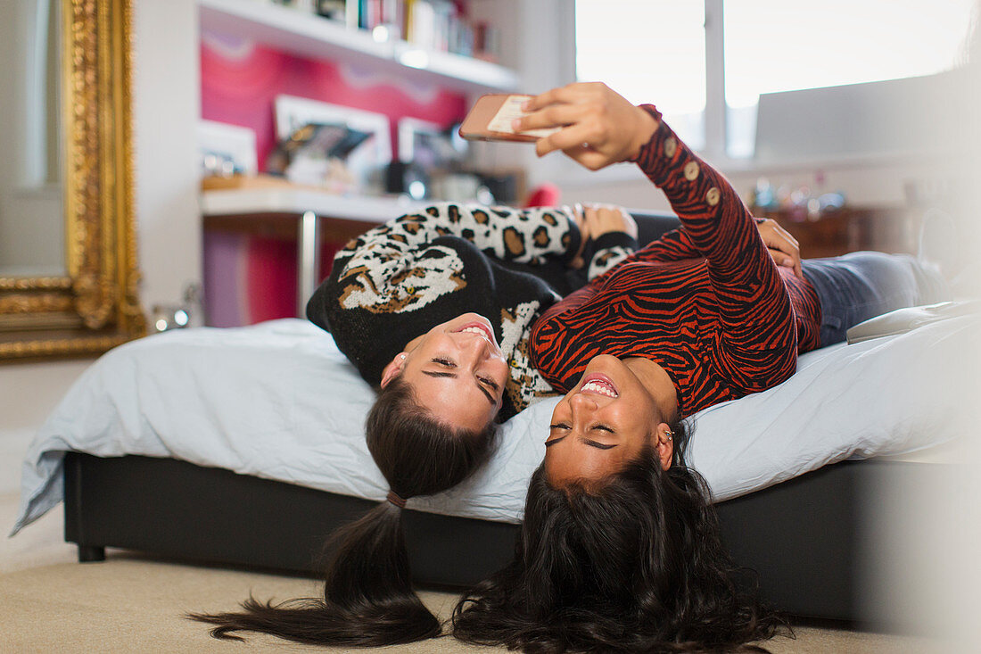 Happy teenage girls taking selfie upside-down on bed