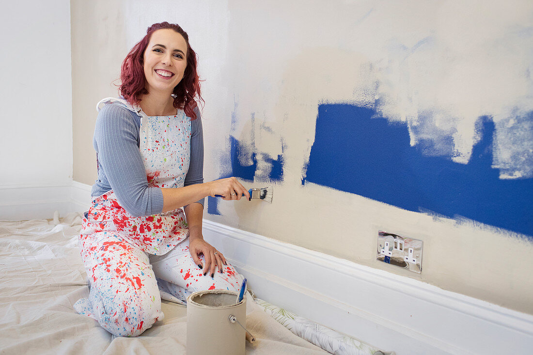 Portrait happy woman in overalls painting wall