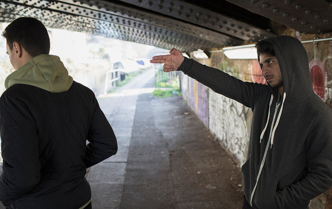 Menacing man gesturing finger gun at man in urban tunnel