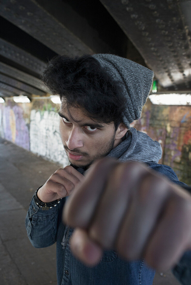 Portrait tough young man punching in urban tunnel