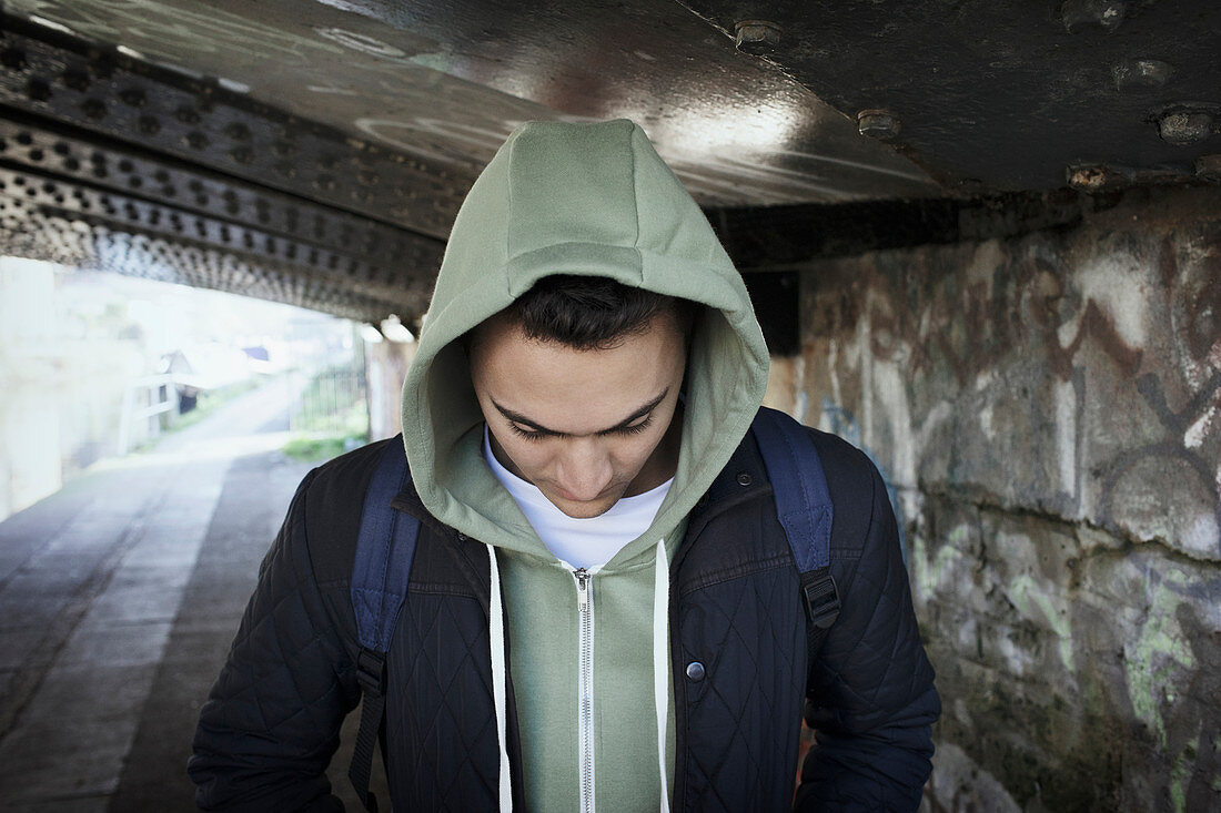 Young man in hoody walking under urban bridge