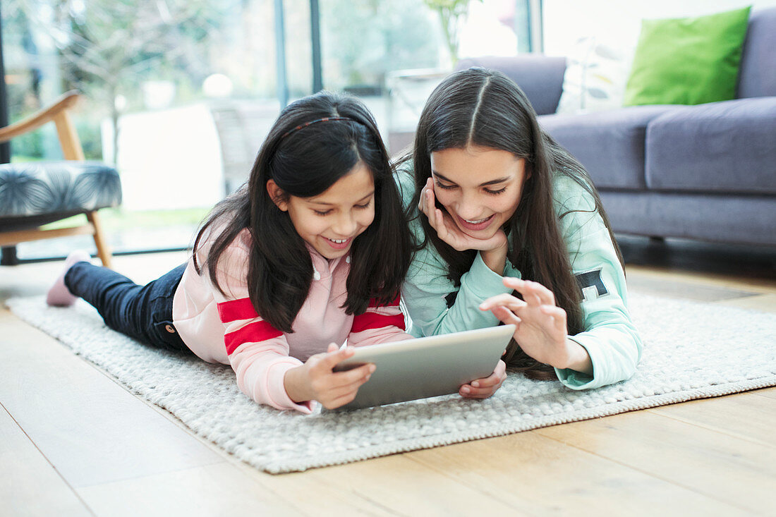 Smiling sisters using digital tablet on living room floor
