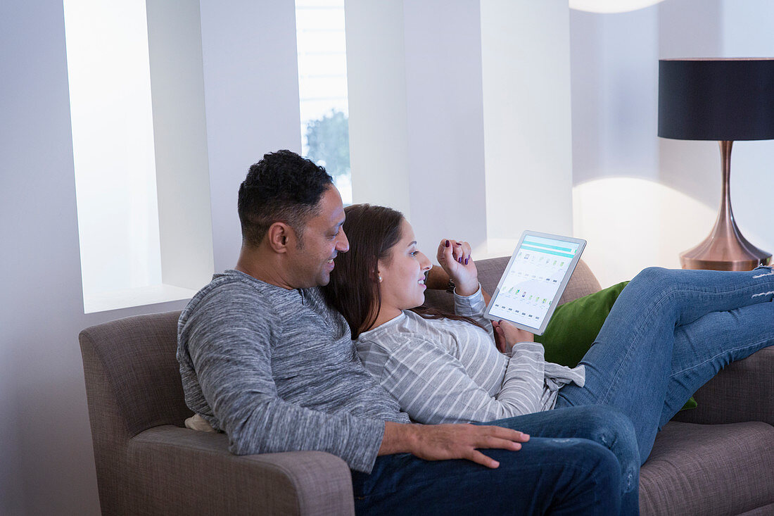 Couple relaxing, using digital tablet on living room sofa