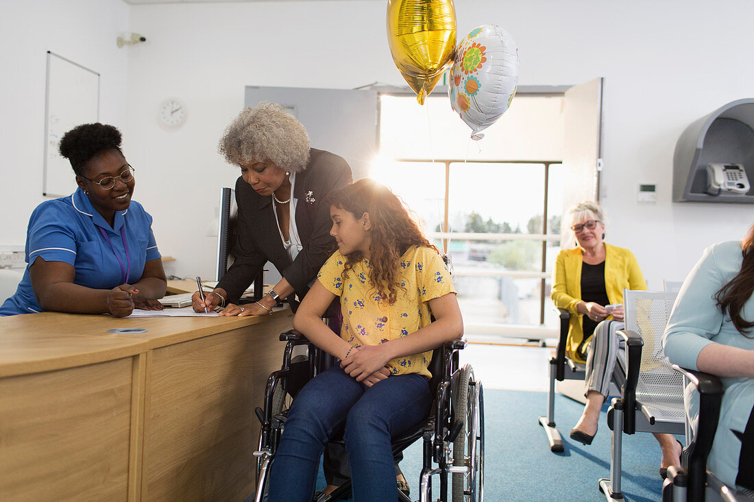 Girl patient in wheelchair checking in at clinic reception