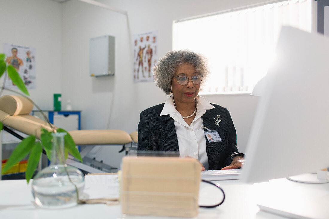 Female senior doctor working at computer in doctors office