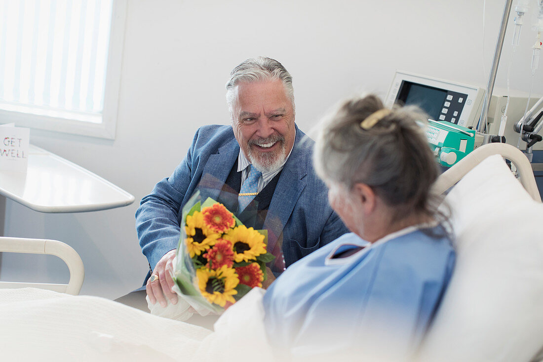 Senior man with flower bouquet visiting wife in hospital