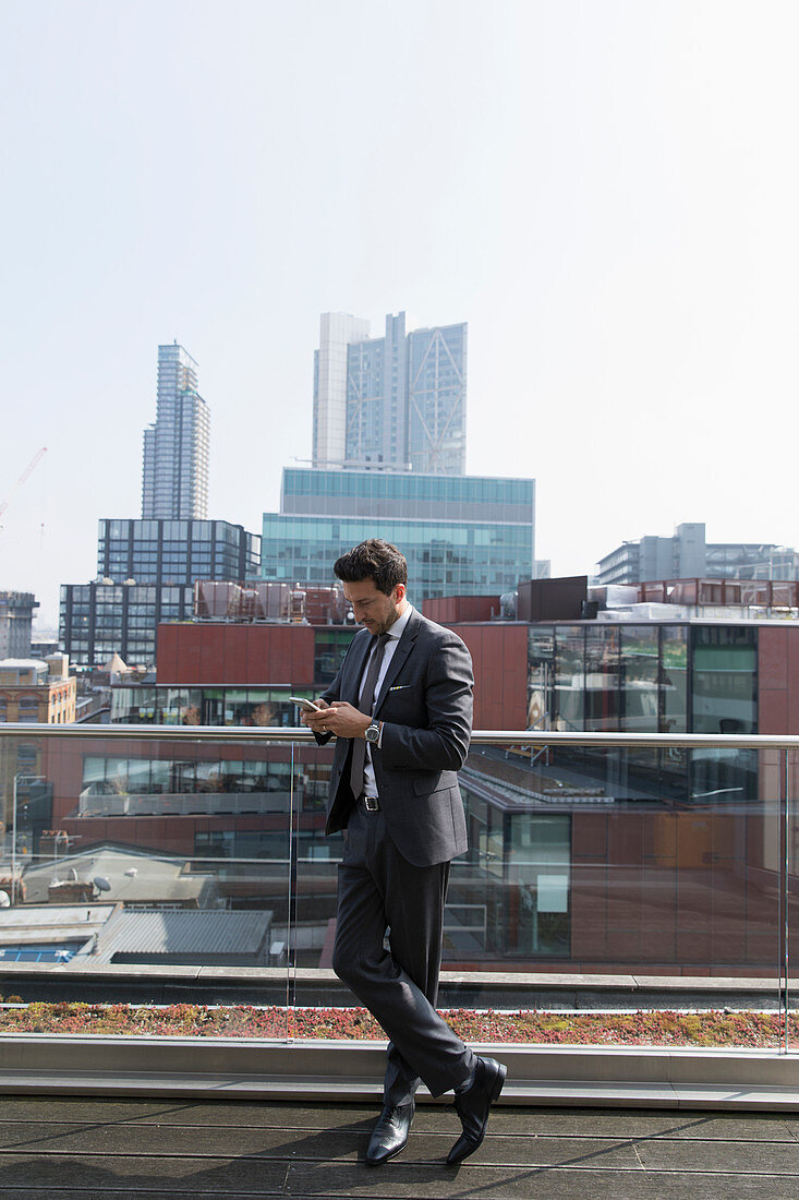 Businessman using smart phone on highrise balcony