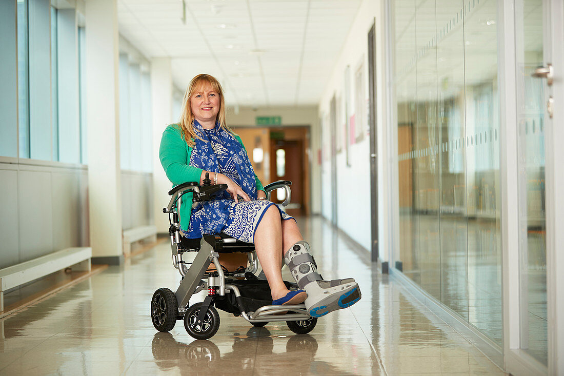 Woman wearing medical boot in wheelchair in corridor