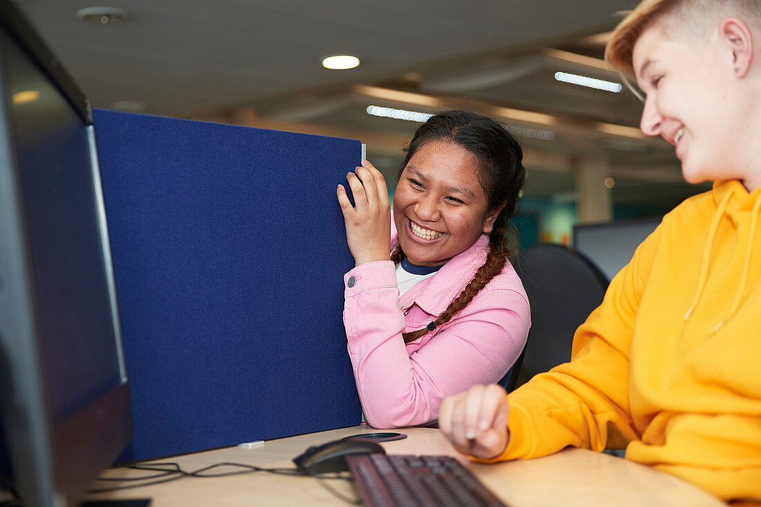 Happy college students laughing at computer in library