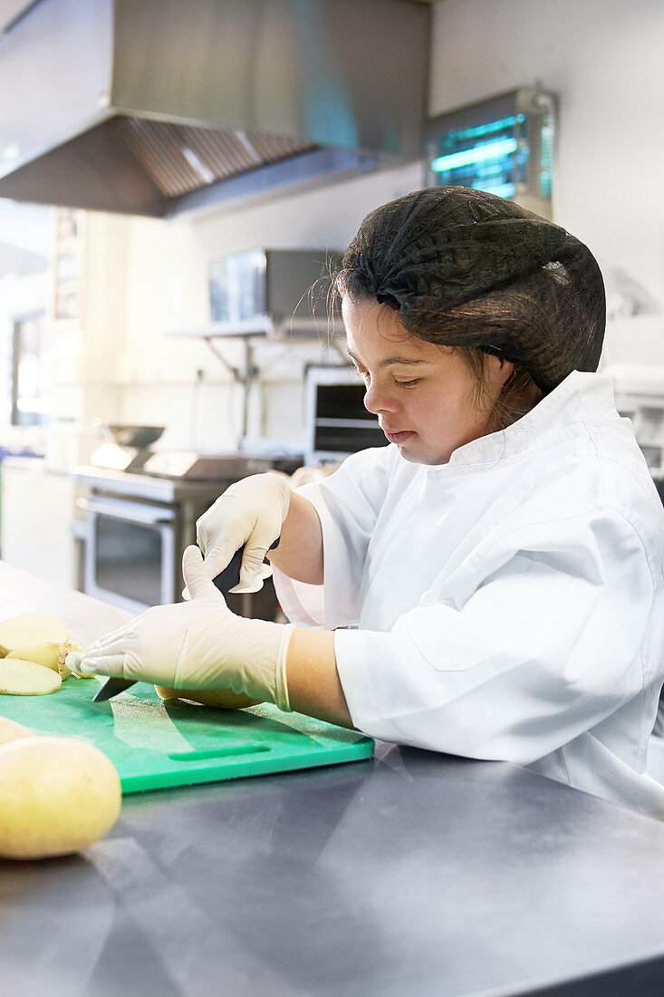 Focused woman with Down Syndrome cooking in cafe kitchen