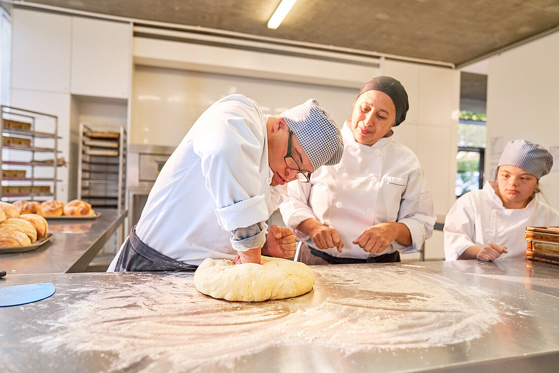 Chef guiding student with Down Syndrome kneading dough