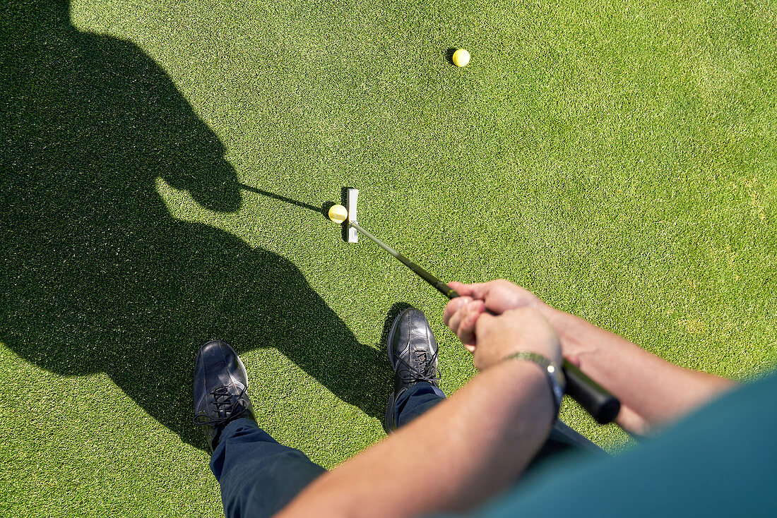 Point of view man putting golf ball on sunny greens