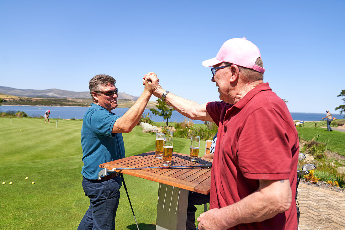 Happy male golfer friends high fiving and drinking beers
