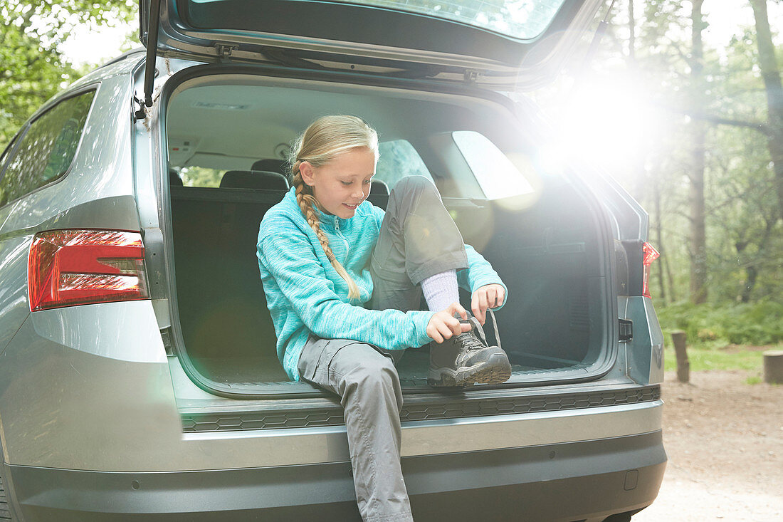 Girl preparing for hike at back of car tying shoes