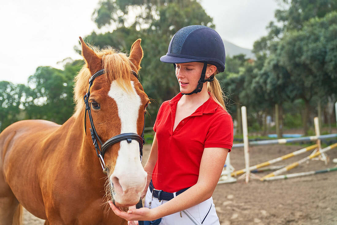 Teenage girl in equestrian helmet with horse in paddock