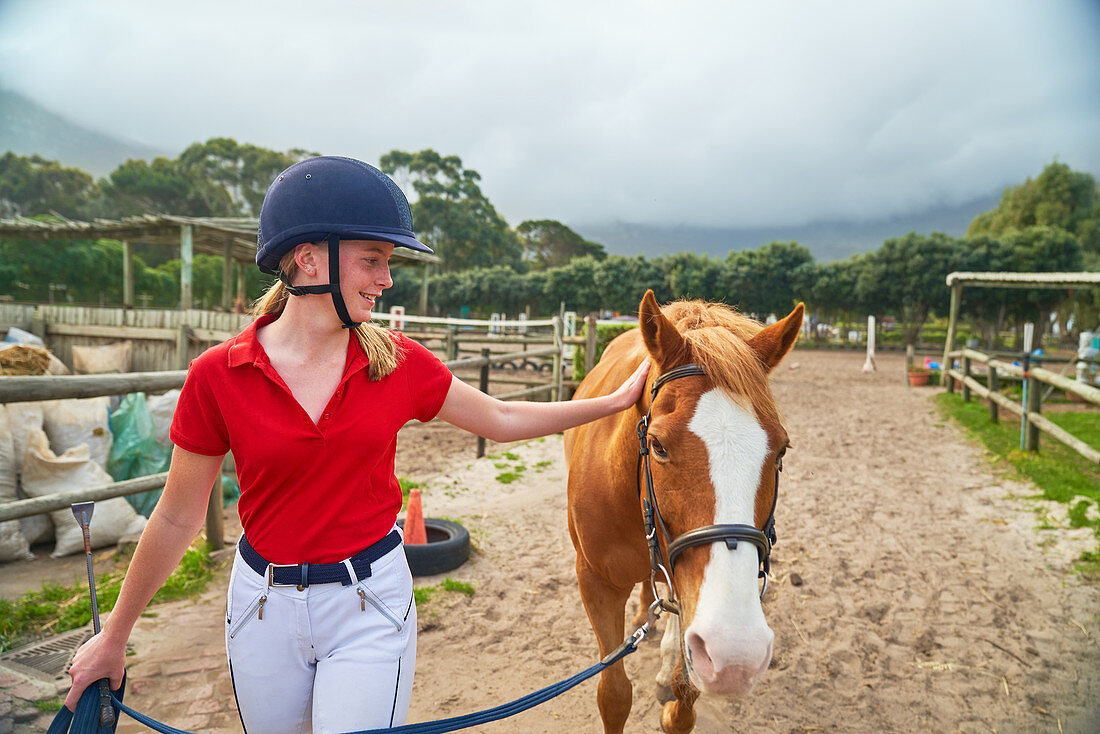 Girl in equestrian helmet leading horse along paddock