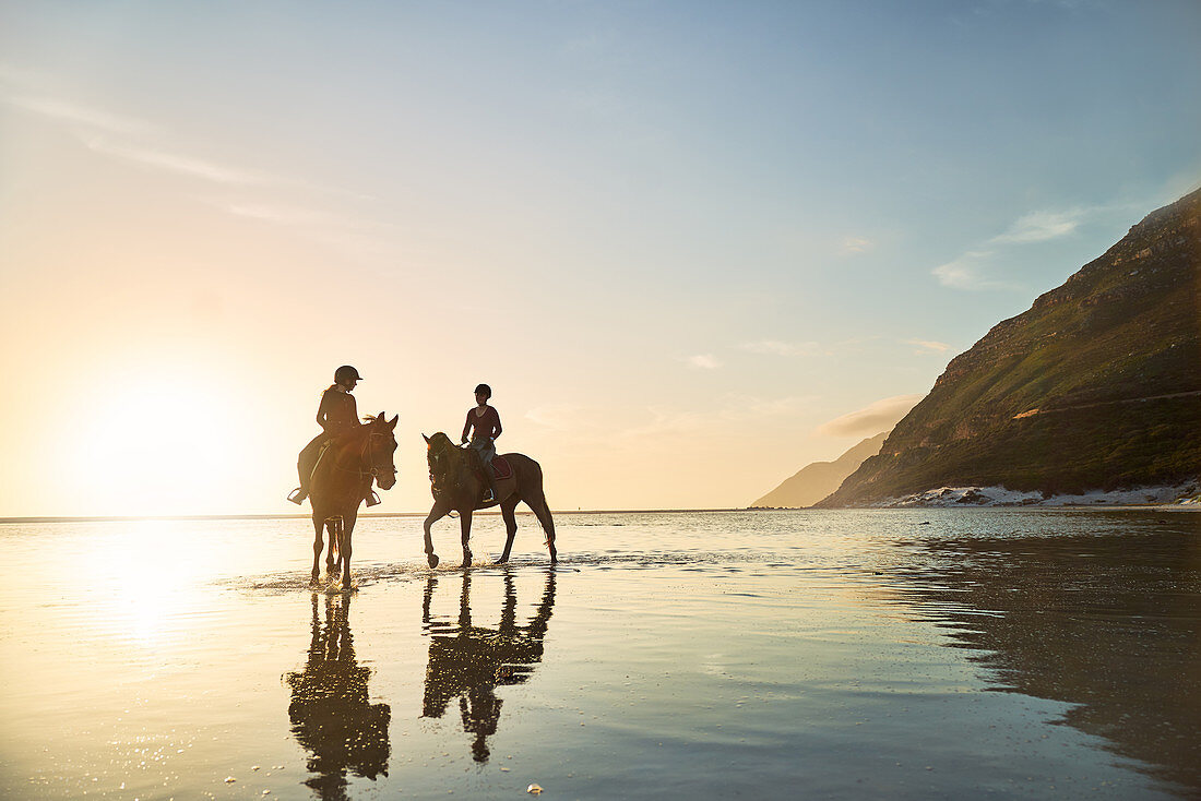 Women horseback riding in tranquil ocean surf at sunset