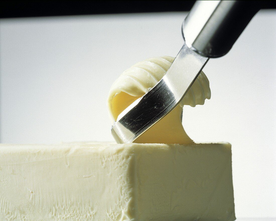 Butterroller zieht ein Butterröllchen von einem Stück Butter