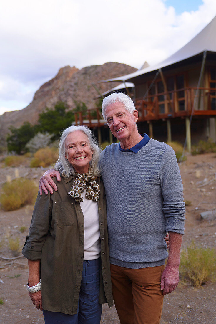 Portrait happy senior couple outside safari lodge cabin