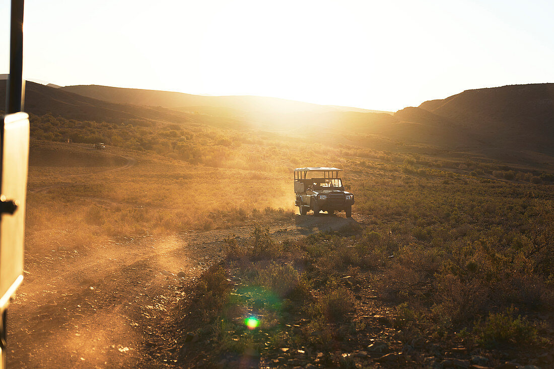 Safari vehicle driving on sunny dirt road South Africa