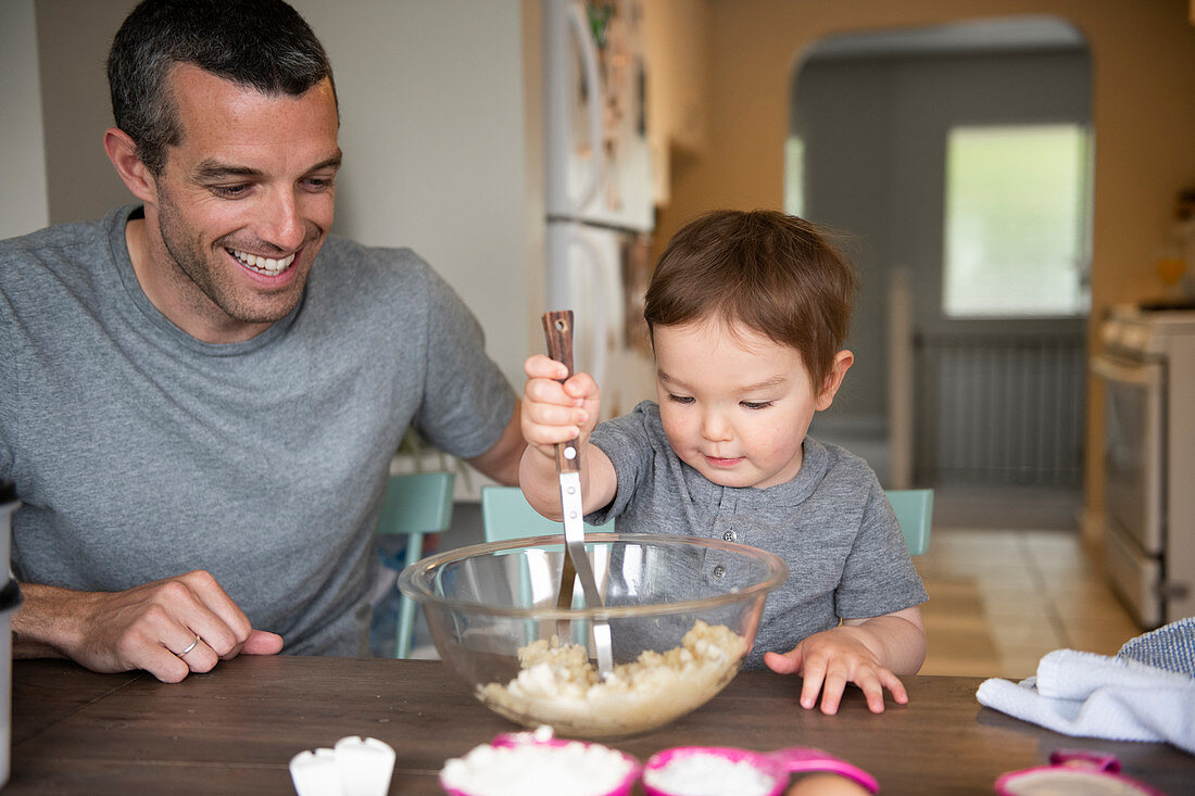 Happy father and toddler daughter baking at kitchen table