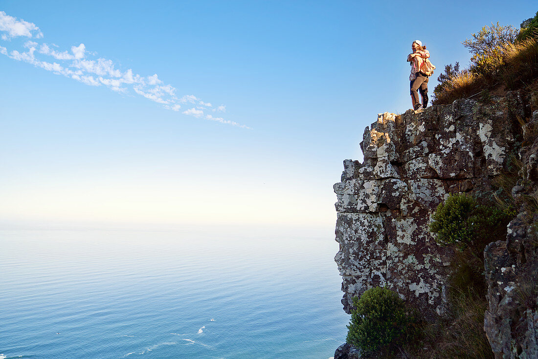 Couple hugging on cliff over sunny ocean