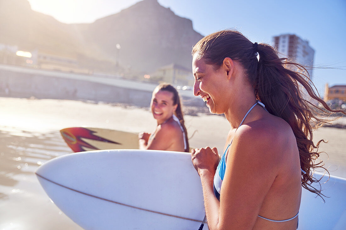 Happy young women friends with surfboards on sunny beach