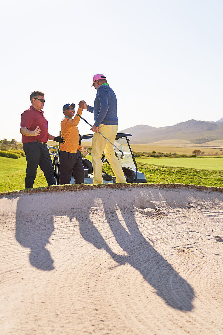 Male golfers celebrating behind sunny golf bunker