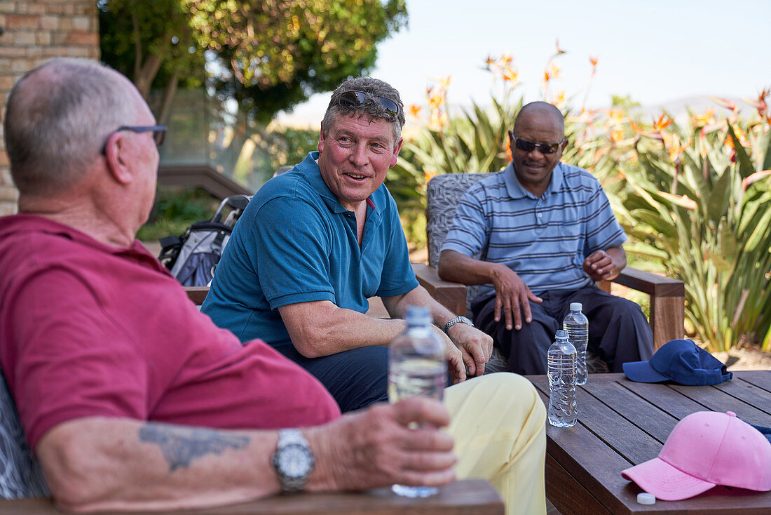 Mature golfer friends talking and drinking water on patio