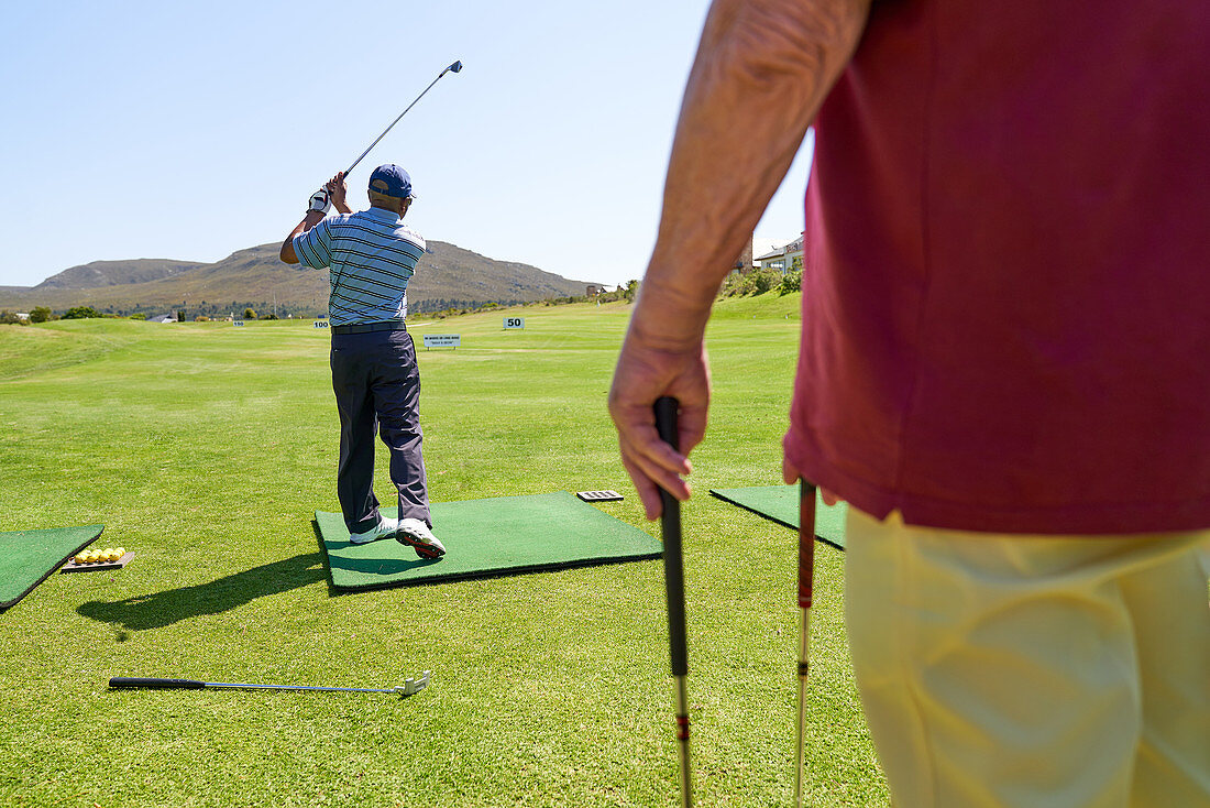 Male golfer practicing at sunny golf course driving range