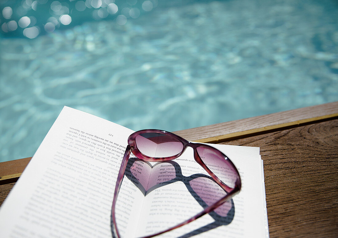 Heart-shape sunglasses on book at poolside