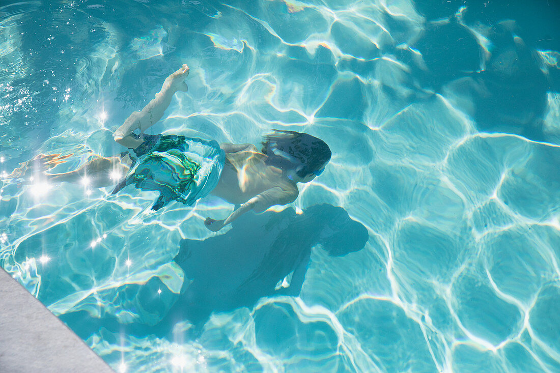 Boy swimming underwater in summer swimming pool