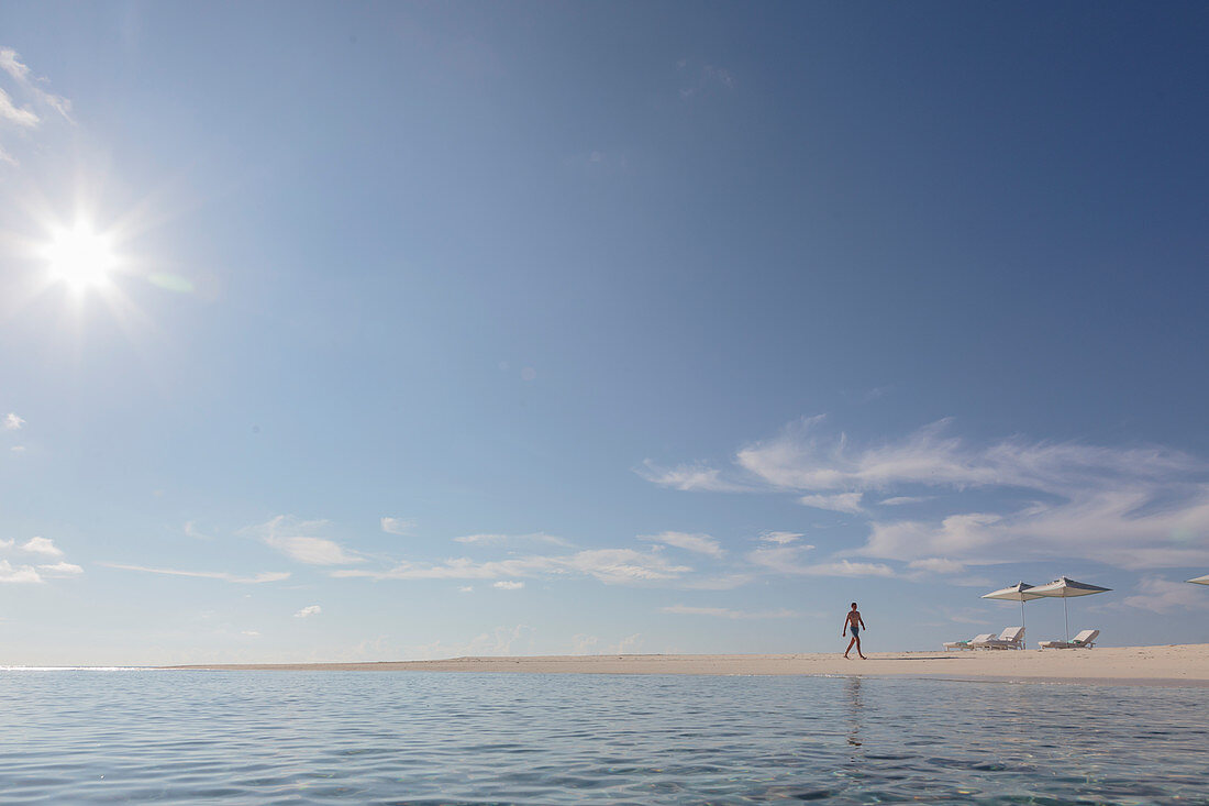 Man walking on sunny, tranquil, remote ocean beach