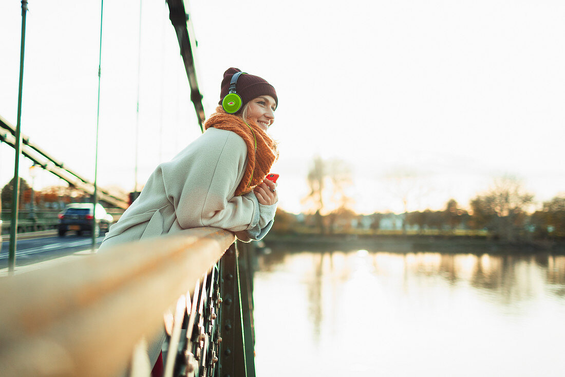 Woman listening to music with headphones on autumn bridge