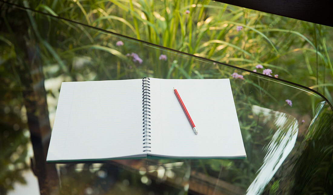 Open blank notebook and pencil on glass table