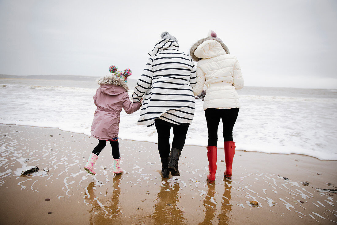 Mother and daughters walking on winter ocean beach