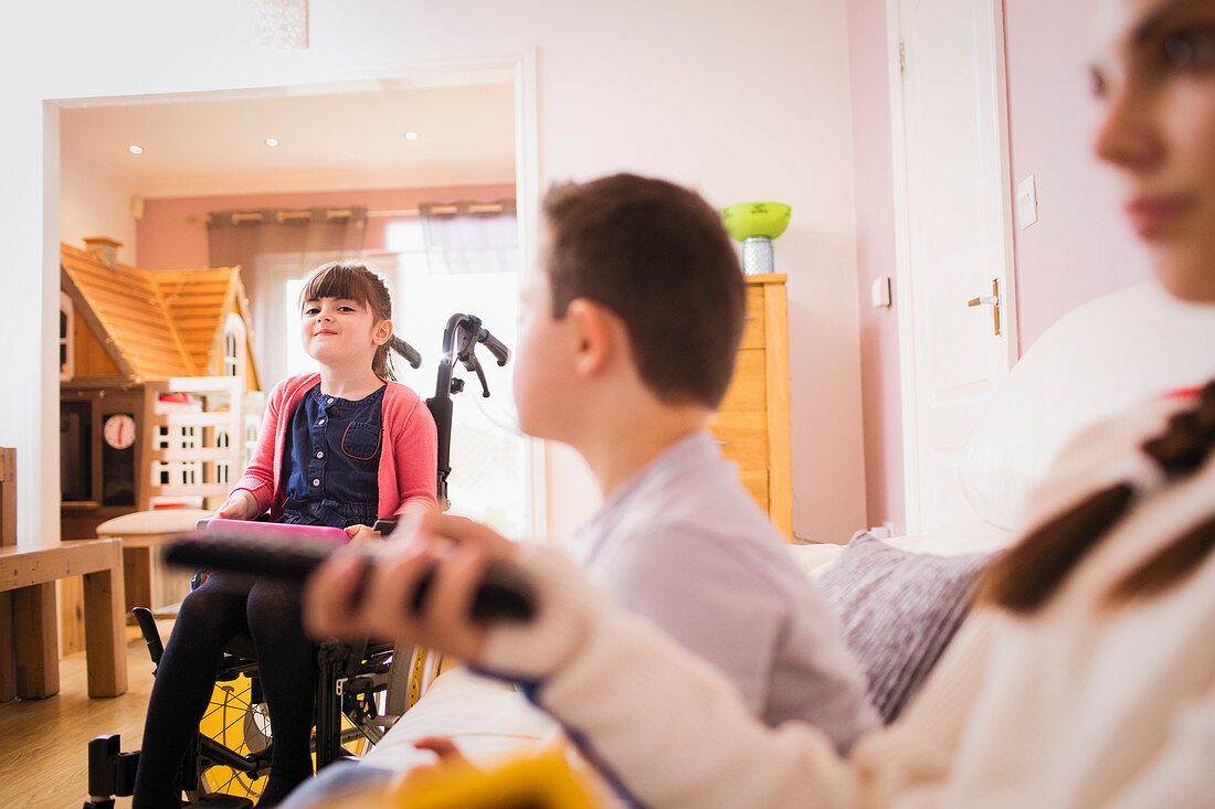 Happy girl in wheelchair with siblings at home