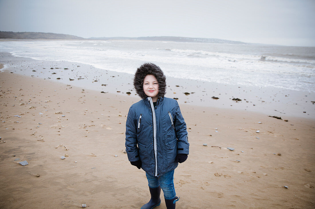 Portrait boy in fur hooded jacket on winter ocean beach