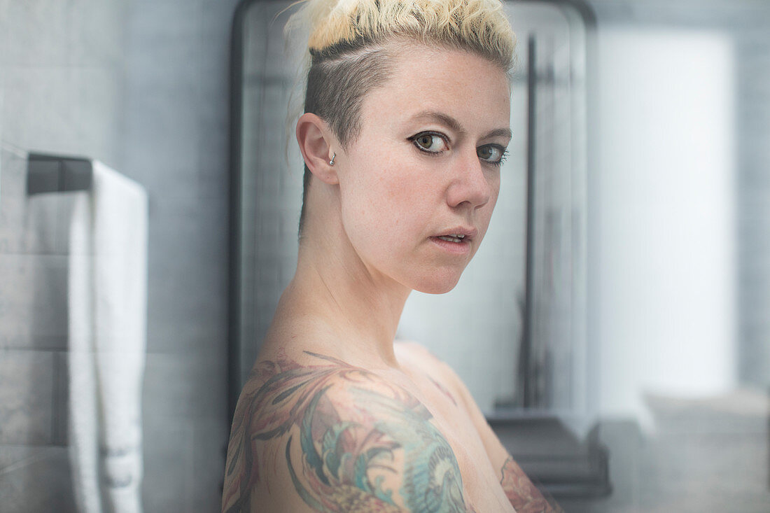 Woman with tattoos and bare shoulders in bathroom