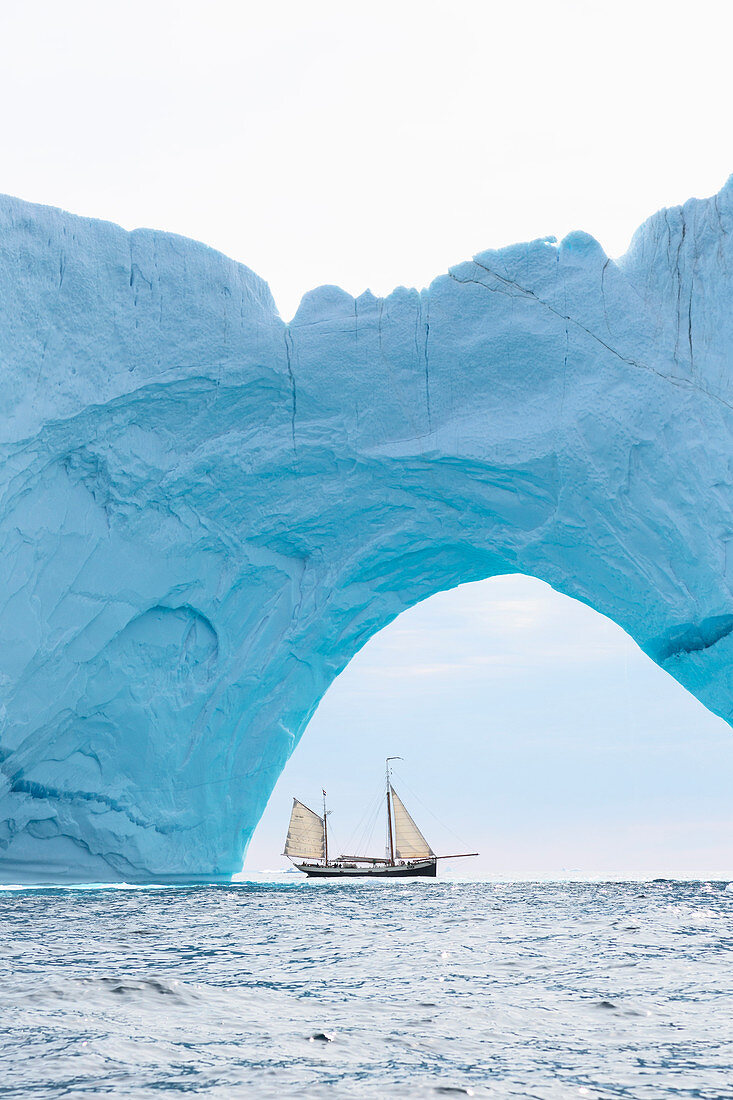 Ship sailing behind iceberg arch on