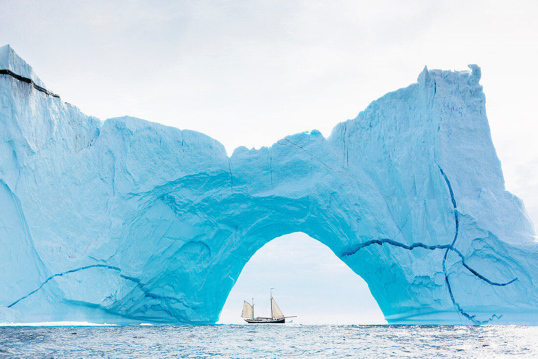 Ship sailing behind majestic iceberg arch on