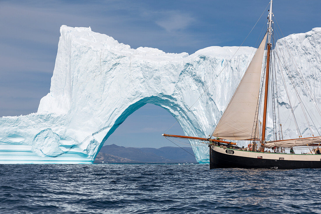 Ship sailing past majestic iceberg arch on ocean Greenland
